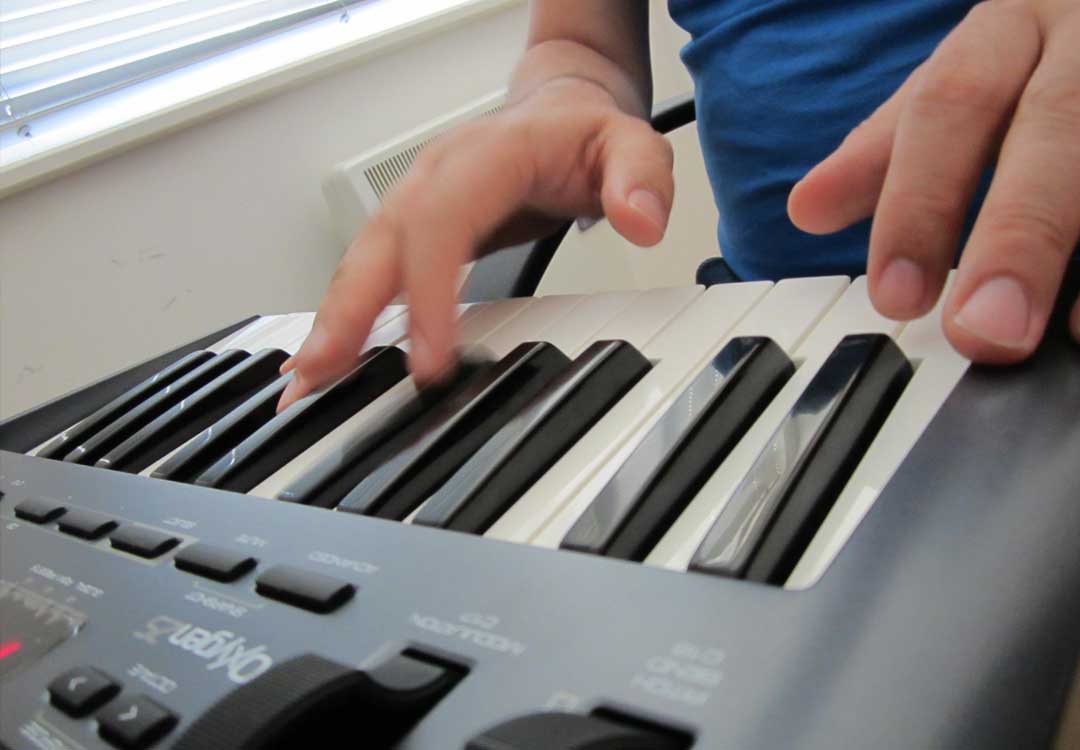 Close up cropped photo of Sawtooth & Sine playing an Oxygen 25 keyboard while sat in a chair. Just the hands and they keys are visible.